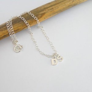 May include: A silver chain anklet with a silver charm that has the letters 'D' and 'S' on it.