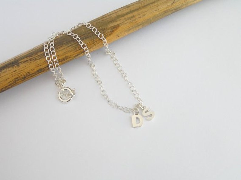 May include: A silver chain anklet with a silver charm that has the letters 'D' and 'S' on it.