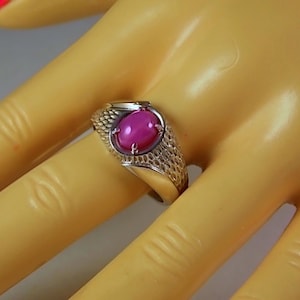 May include: A silver ring with a large, oval, pink gemstone. The ring has a textured band and a decorative setting around the stone. The gemstone is the focal point, with a polished, reflective surface.
