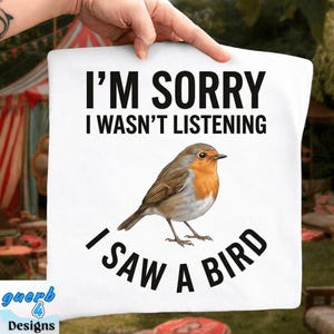 May include: White square pillow with the text "I'M SORRY I WASN'T LISTENING I SAW A BIRD" and a detailed illustration of a robin. The bird has brown, orange, and white feathers. The pillow is held by a hand.
