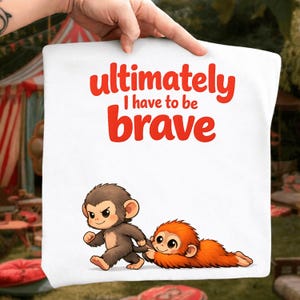 Op de afbeelding: Witte draagtas met de rode tekst "Ultimately I have to be brave". De tas heeft een cartoon illustratie van twee apen, een bruine en een oranje. De bruine aap loopt en trekt de oranje aap.