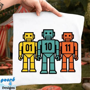 May include: White pillowcase featuring three cartoon robots in yellow, teal, and orange. Each robot has a number: 01, 10, and 11. The pillowcase has the text "guerb 4 Designs" in the bottom left corner.