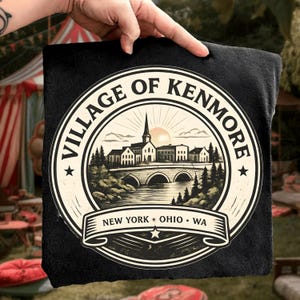 Puede incluir: Cuadrado negro con un diseño circular. El texto "VILLAGE OF KENMORE" rodea una ilustración detallada de un pueblo con un puente, un río y árboles. El texto "NEW YORK * OHIO * WA" está debajo.