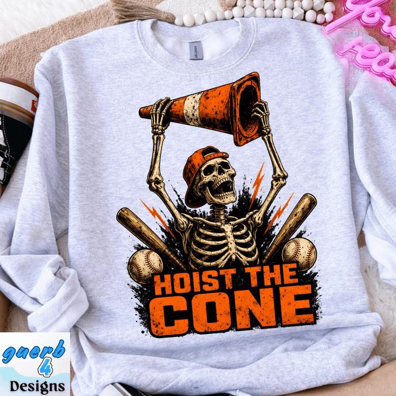 May include: A light gray sweatshirt with a graphic featuring a skeleton wearing a baseball cap and holding a traffic cone. The text "HOIST THE CONE" is below the skeleton, with baseballs and bats on either side.