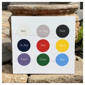 May include: A white wooden board with nine painted circles, each labeled with a color name: Ivory, Lt. Gray, Black,  Dk. Blue, Red, Yellow, Purple, Green, and Blue.
