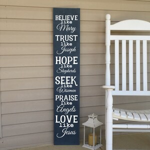 Op de afbeelding: Een donkerblauw houten bord met witte tekst die luidt: "BELIEVE like Mary, TRUST like Joseph, HOPE like Shepherds, SEEK like Wisemen, PRAISE like Angels, LOVE like Jesus".