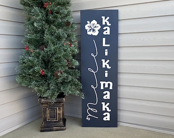 May include: A black wooden sign with white lettering that reads "Welcome" in a cursive font and "Kailua-Kona" in a block font. The sign is decorated with a white hibiscus flower.