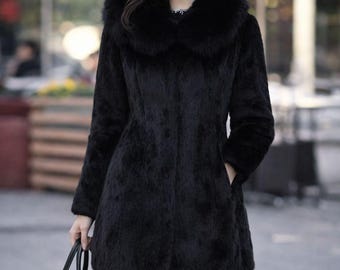 May include: A black faux fur coat with a large collar. The coat is knee-length and has long sleeves. A black handbag with gold-colored hardware is held in the hand. The coat is worn with black tights.