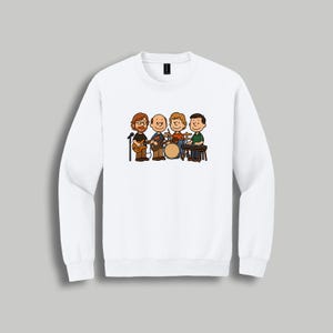 May include: White crewneck sweatshirt featuring a cartoon band illustration. The band consists of four characters playing guitar, drums, and keyboard. The illustration is in a simple, colorful style, with the band members in various outfits.