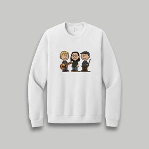 May include: White sweatshirt featuring a cartoon illustration of three characters playing musical instruments. One character plays a guitar, another a ukulele, and the third holds a conductor's baton. The characters are in a line, with a neutral background.