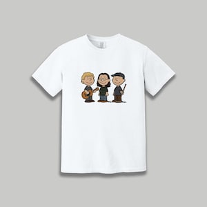 May include: White t-shirt featuring a cartoon illustration of three characters. One character is playing a guitar, another is wearing glasses, and the third is holding drumsticks. The characters are in a line, with a neutral background.