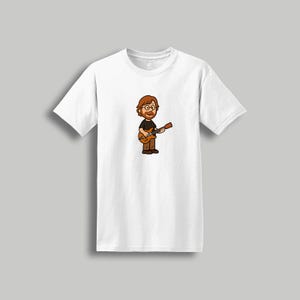 May include: White t-shirt featuring a cartoon illustration of a person with glasses, a beard, and a black shirt playing a brown guitar. The design is centered on the front of the shirt, with the sleeves and collar visible.