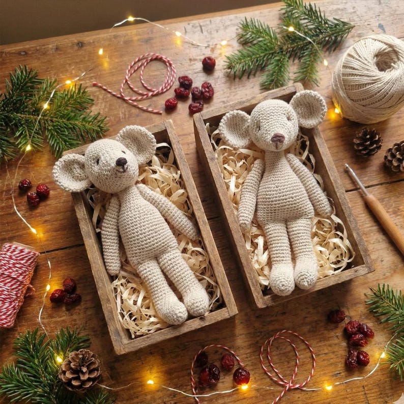 Puede incluir: Dos mu&ntilde;ecos de rat&oacute;n de ganchillo beige en cajas de madera llenas de paja. Los ratones tienen orejas grandes y ojos negros peque&ntilde;os. Las cajas est&aacute;n sobre una superficie de madera con agujas de pino, cuerda y bayas secas.