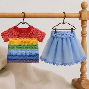 Puede incluir: Una camiseta de ganchillo de manga corta con rayas horizontales en rojo, naranja, amarillo, verde, azul claro y morado, junto a una falda de tul azul claro con cintura de ganchillo y dobladillo festoneado, ambas colgadas en perchas.