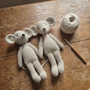 Puede incluir: Dos ratones hechos a mano con ganchillo en color beige claro. Los ratones tienen orejas grandes y redondeadas, ojos negros peque&ntilde;os y colas largas. Tambi&eacute;n se ven una madeja de hilo y un ganchillo.