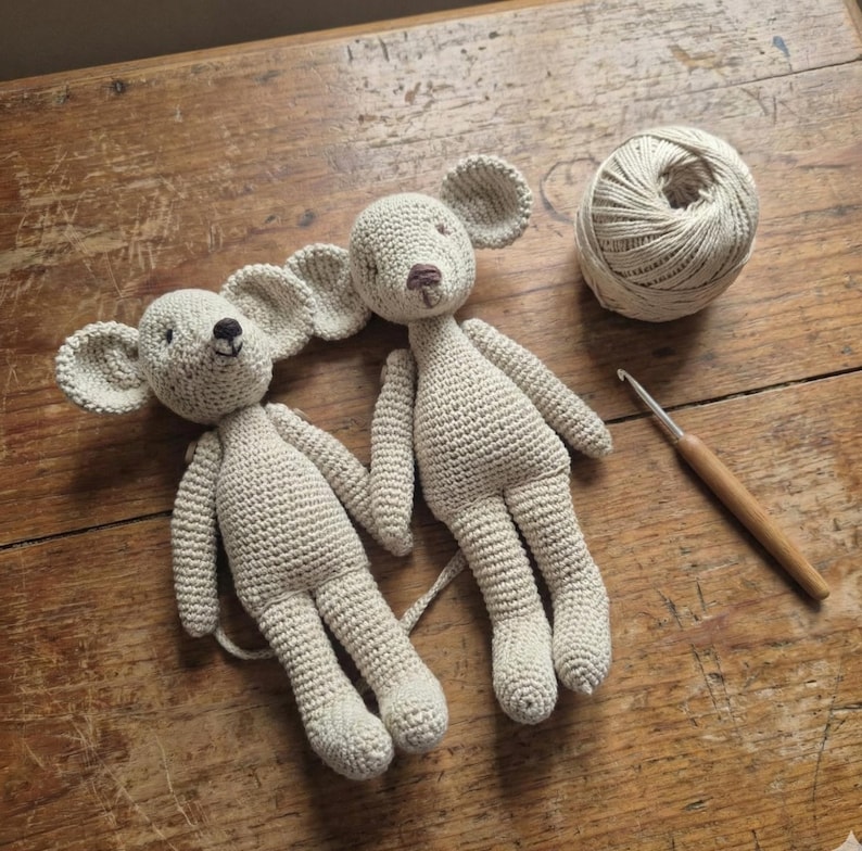 Puede incluir: Dos ratones hechos a mano con ganchillo en color beige claro. Los ratones tienen orejas grandes y redondeadas, ojos negros peque&ntilde;os y colas largas. Tambi&eacute;n se ven una madeja de hilo y un ganchillo.