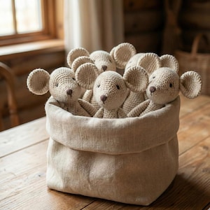 Puede incluir: Un grupo de ratones de ganchillo beige con orejas grandes, metidos en una bolsa de lino a juego. Los juguetes hechos a mano se exhiben sobre una superficie de madera, creando una est&eacute;tica r&uacute;stica y acogedora.