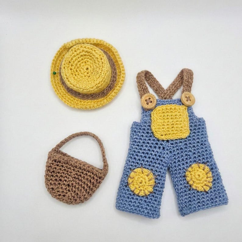 May include: A crochet set featuring a yellow and brown hat, a small brown purse, and blue overalls with yellow patches. The overalls have brown straps and wooden button details. The set is handmade.