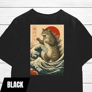 May include: Black t-shirt featuring a graphic of a cat resembling Godzilla, with a red sun in the background and Japanese text. The cat is depicted in a dynamic pose amidst stylized ocean waves.