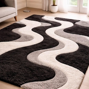 May include: A rectangular rug featuring a flowing, wavy design in black, white, and grey. The rug has a soft, textured pile and is placed on a wooden floor. The abstract pattern adds a modern touch to the room.
