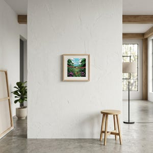 May include: A square framed art print featuring a vibrant landscape illustration with a central rectangular window showing a small house, surrounded by lush green trees, purple flowers, and a bright blue sky with white clouds, all encased in a light wood frame.