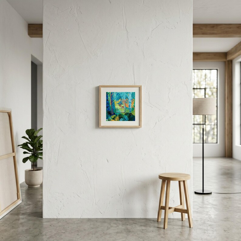 May include: A square framed art print featuring a vibrant jungle scene with deep blue, green, and yellow tones, displayed on a white wall. The artwork depicts dense foliage and trees, centered within a light-colored wooden frame.