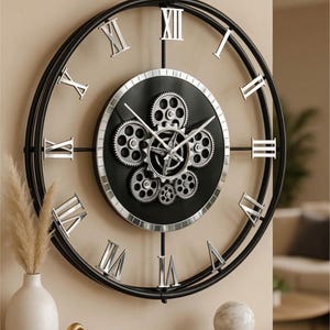 May include: A large, black and silver wall clock with a gear design. The clock face is black with silver gears and Roman numerals. The clock measures 60 x 70 cm.