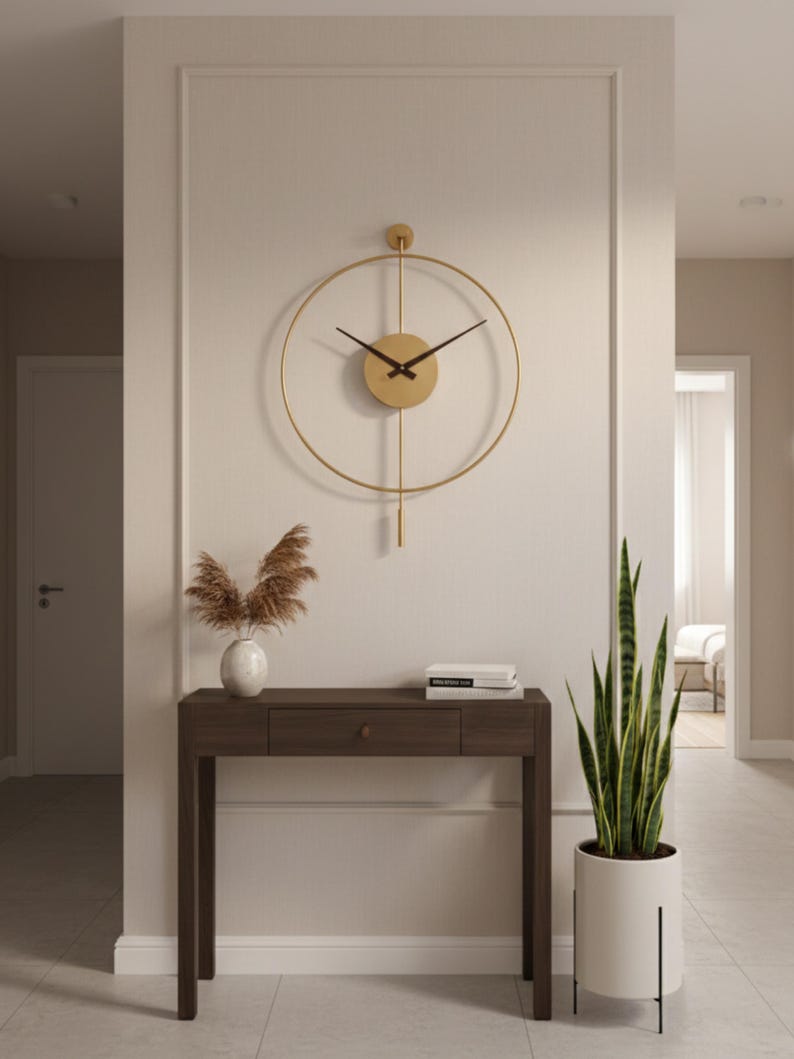 K&ouml;nnte beinhalten: Eine goldfarbene, kreisf&ouml;rmige Wanduhr mit schwarzen Zeigern h&auml;ngt &uuml;ber einem dunklen Holzkonsolentisch. Eine wei&szlig;e Vase mit getrockneten Pflanzen und ein Stapel B&uuml;cher stehen auf dem Tisch. Rechts steht eine hohe Topf-Schlangenpflanze.