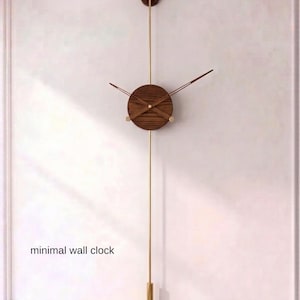 Può includere: Un orologio da parete minimalista con quadrante in legno e dettagli color oro. L'orologio è lungo 80 cm e presenta un design a pendolo. Il testo "STATEMENT SIZE 80 cm | 31.5" è visibile. Le parole "minimal wall clock" sono anch'esse visibili.