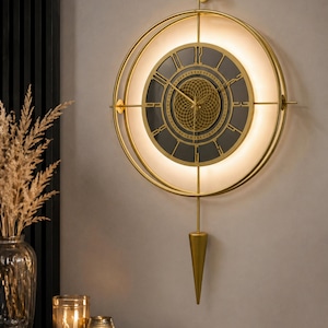 Puede incluir: Un reloj de pared circular de color dorado con esfera negra y números romanos. El reloj tiene un anillo luminoso blanco brillante alrededor de la esfera y un péndulo dorado. El reloj está montado en una pared de color neutro.