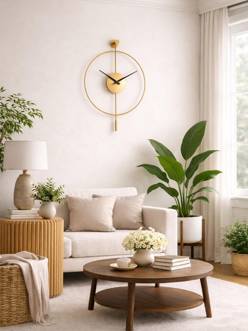 K&ouml;nnte beinhalten: Eine goldfarbene, minimalistische Wanduhr mit schwarzen Zeigern h&auml;ngt an einer wei&szlig;en Wand. Die Uhr hat einen kreisf&ouml;rmigen Rahmen und ein Pendel. Der Raum verf&uuml;gt &uuml;ber ein wei&szlig;es Sofa, einen runden Couchtisch aus Holz und verschiedene Pflanzen.