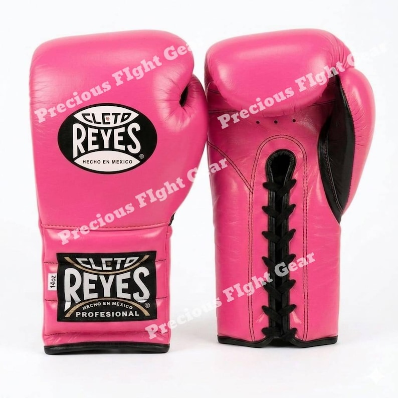 May include: A pair of bright pink boxing gloves with black lace-up closures. The gloves feature the Cleto Reyes logo in black and white ovals, with the text '14oz' and 'Hecho en Mexico' printed on the wrist area of the left glove.