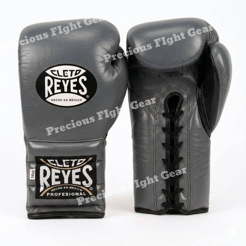 May include: A pair of grey leather boxing gloves featuring black laces and the Cleto Reyes logo on the wrist and back of the hand. The gloves are marked with 14oz on a small white tag. The text Cleto Reyes Hecho en Mexico is visible.