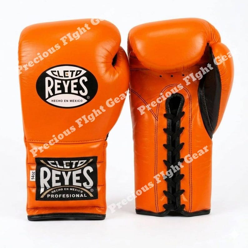 May include: A pair of bright orange boxing gloves featuring black lace-up closures and black trim. The gloves display the Cleto Reyes logo in black and white on the wrist and back of the hand, with the text 14oz clearly visible on the wrist label.