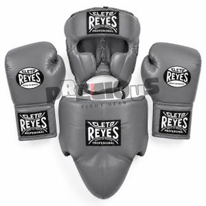 Peut inclure: Un ensemble d'équipement de boxe gris comprenant deux gants de boxe, un casque et une coquille de protection. Chaque pièce comporte une étiquette noire et blanche Cleto Reyes avec le texte Cleto Reyes Hecho en Mexico Profesional imprimé.