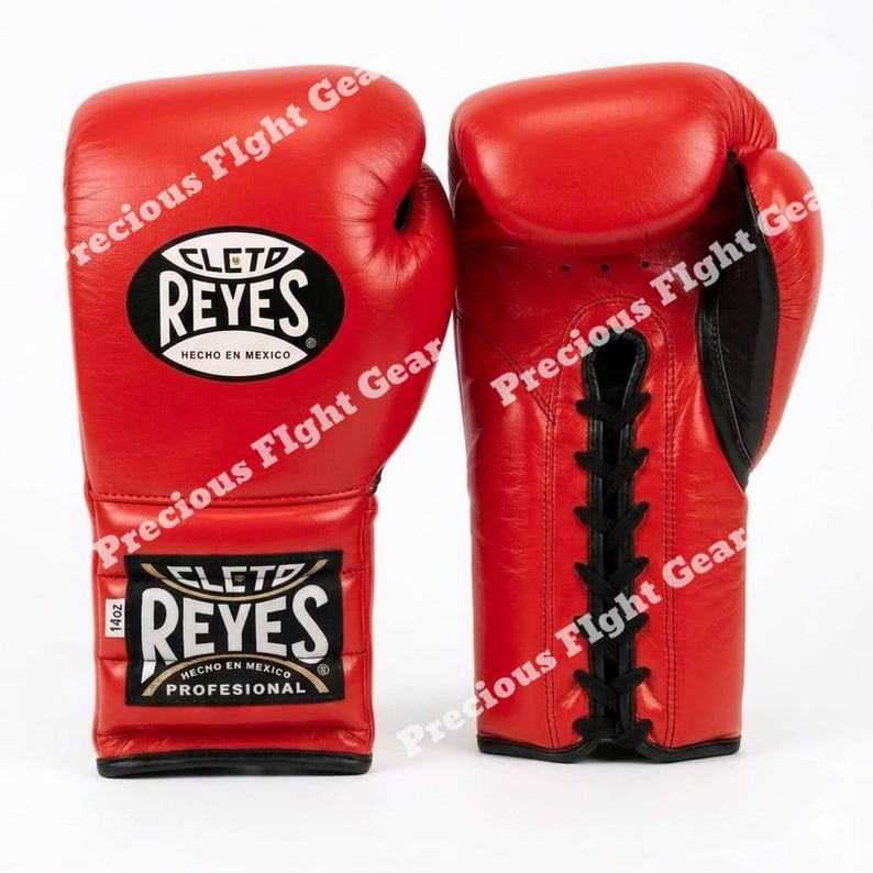 May include: A pair of bright red Cleto Reyes boxing gloves featuring black lace-up closures and black logo patches. The gloves display the text Cleto Reyes Hecho en Mexico and 14oz on the wrist area. The design includes black accents on the palm side.