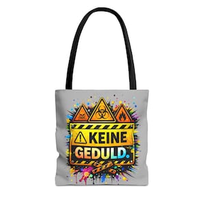 Könnte beinhalten: Eine graue Tragetasche mit schwarzem Griff zeigt ein farbenfrohes Design. Das Design umfasst Gefahrensymbole und den Text "KEINE GEDULD" in Gelb und Schwarz. Die Tasche hat einen Farbspritzer-Effekt.