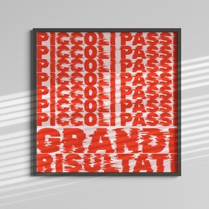 May include: A framed art print with a white background and red text. The text includes the words "PICCOLI PASS" repeated vertically, and "GRANDI RISULTATI" at the bottom. The frame is black.