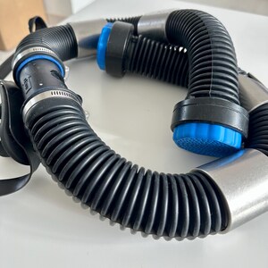 Peut inclure: Gros plan sur un tuyau noir ondulé avec des connecteurs métalliques argentés et des détails bleus. Le tuyau est courbé et semble faire partie d'un système plus large.