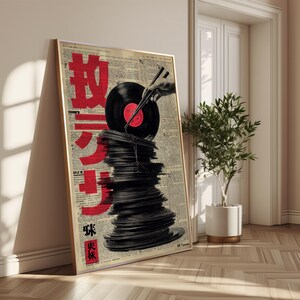 May include: A framed art print featuring a stack of black vinyl records with a red label, topped by a single record held by chopsticks. The background is a collage of newspaper clippings with large red Japanese characters.