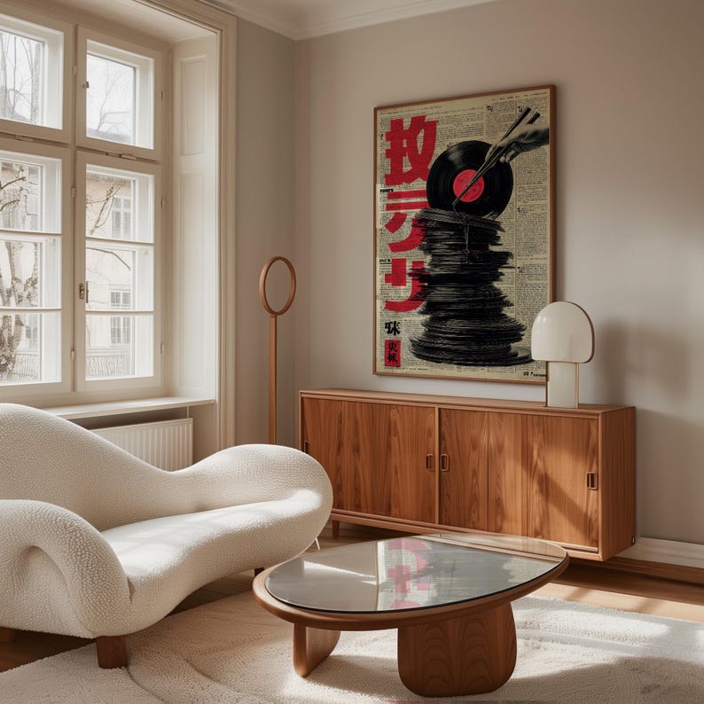 May include: A framed poster featuring a stack of vinyl records with a record player arm and Japanese text in red. The poster is displayed above a wooden cabinet, with a white lamp and a modern, curved sofa in the foreground.