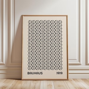 May include: A framed Bauhaus art print featuring a geometric pattern of black cubes on a cream background. The print includes the text "BAUHAUS 1919" in a bold, sans-serif font. The frame is a light brown color.