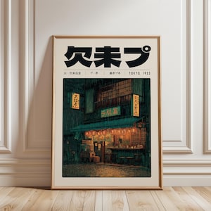 May include: Framed art print featuring a vintage Japanese street scene in Tokyo, 1923. The artwork depicts a rainy night with a shop illuminated by lanterns and signage in Japanese characters. The print is in a wooden frame.