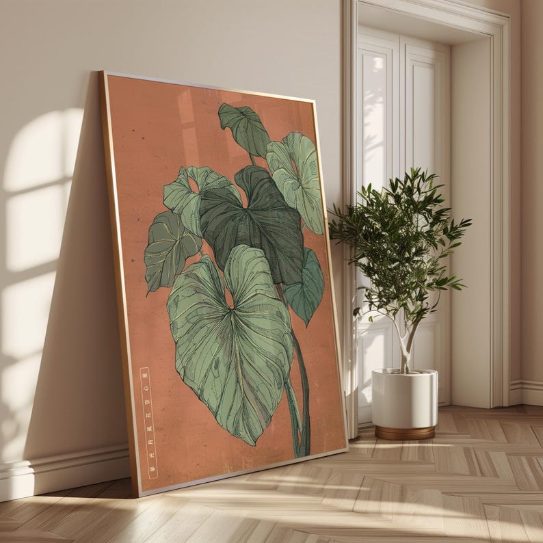 May include: A framed botanical print featuring a detailed illustration of large, green tropical leaves against a muted orange background. The artwork is displayed in a room with a wooden floor and a small potted plant.