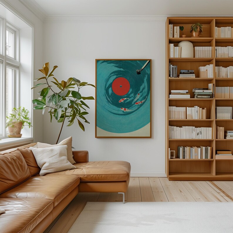 Op de afbeelding: Een ingelijste kunstdruk met een vinylplaatontwerp met een turquoise achtergrond en een rood midden. Het kunstwerk toont koi-karpers die in de groeven van de plaat zwemmen. De print wordt weergegeven in een woonkamer met een leren bank en een houten boekenkast.
