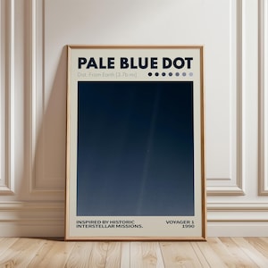 Op de afbeelding: Een ingelijste poster met de tekst "PALE BLUE DOT" en "Dist. From Earth [3.7b mi]" bovenaan. De afbeelding toont een donkerblauwe gradiënt met een lichte streep. De tekst onderaan luidt "INSPIRED BY HISTORIC INTERSTELLAR MISSIONS. VOYAGER 1 1990".