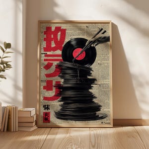 May include: A framed poster featuring a stack of black vinyl records with a red label. A hand holding chopsticks is positioned above the records. Red Japanese characters are printed on the left side of the poster, set against a backdrop of newspaper print.