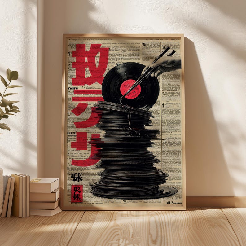 May include: A framed poster featuring a stack of black vinyl records with a red label. A hand holding chopsticks is positioned above the records. Red Japanese characters are printed on the left side of the poster, set against a backdrop of newspaper print.