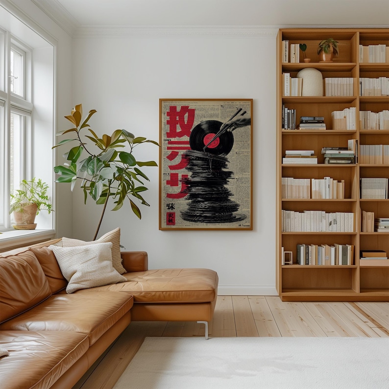 May include: A framed art print featuring a stack of vinyl records with a red and black record on top. The artwork has Japanese text in red and is set against a newspaper background. The print is in a wooden frame.