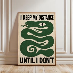 May include: A rectangular wall art print featuring a dark green snake coiled in a serpentine pattern against a cream background. The text I KEEP MY DISTANCE is printed in black at the top, and the text UNTIL I DON'T is printed in black at the bottom.